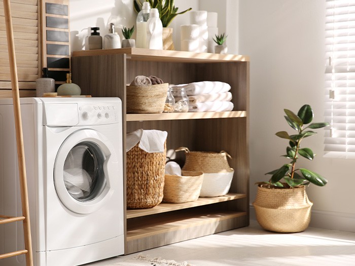 Dryer in laundry room next to shelves with folded towels and baskets.